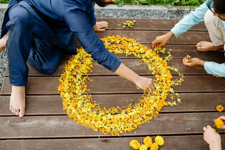 People arranging vibrant yellow petals into a circular floral design on wooden floor.