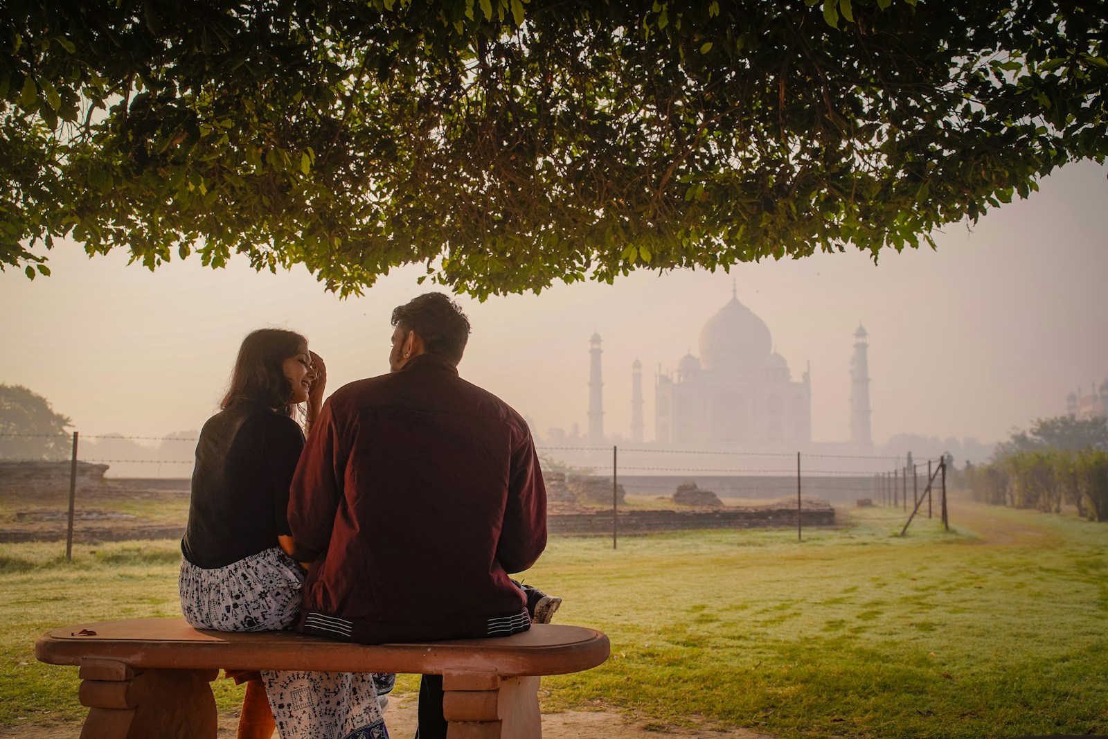 Couple sits on bench, taj mahal in misty background